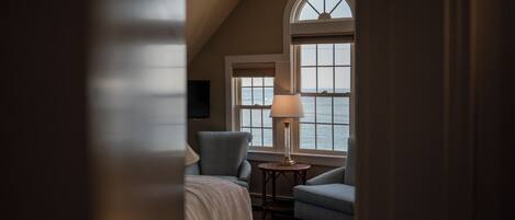 Un dormitorio con una cama, dos sillas, una lámpara y una ventana con vista al mar.