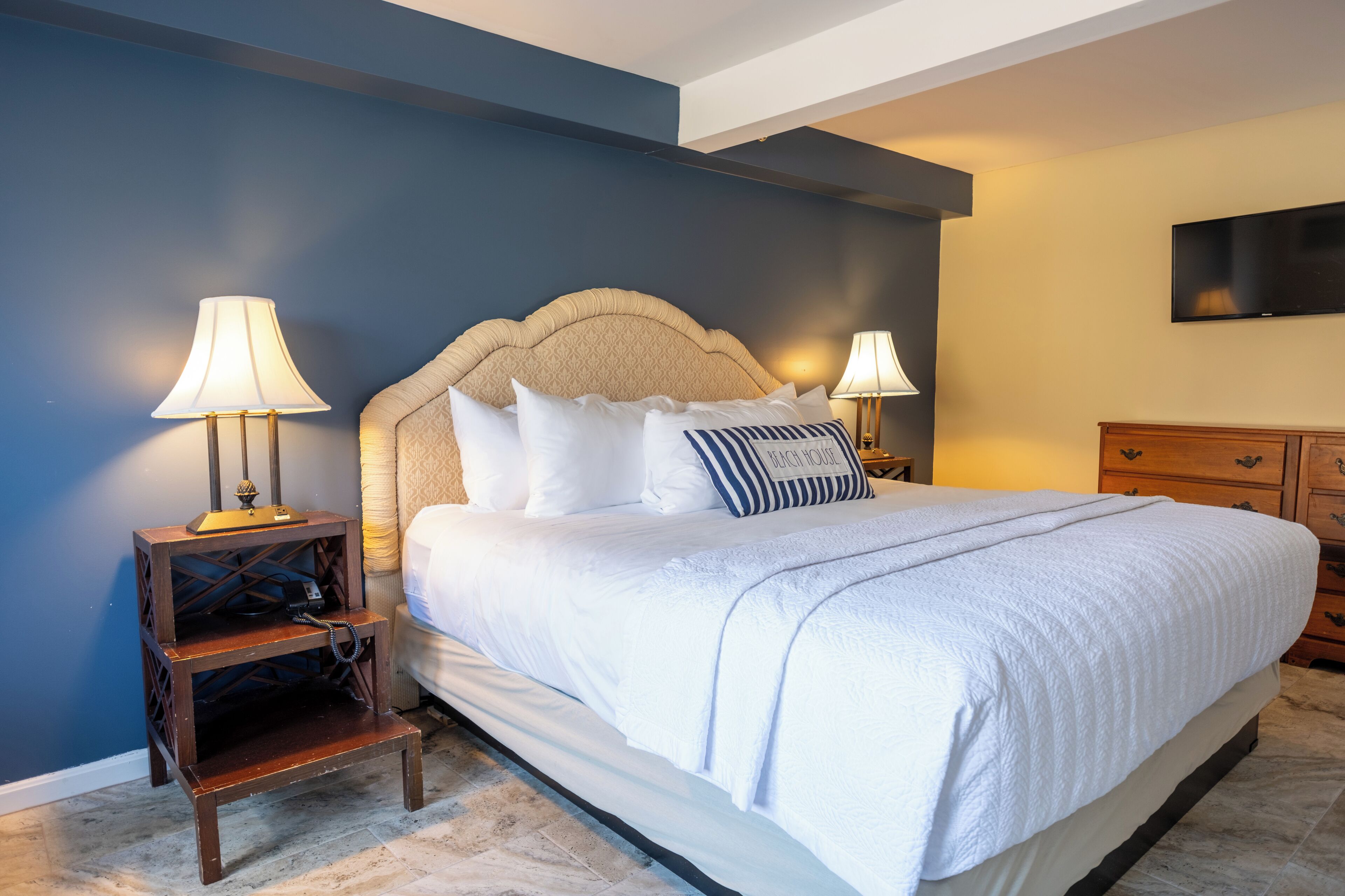 Quarto com uma cama grande, duas mesas de cabeceira com luminárias, uma televisão na parede e um aparador de madeira.