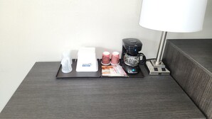 Mesita de noche en una habitación de hotel con cafetera, lámpara y bandeja de artículos de aseo.