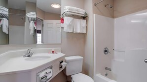 Un baño moderno con lavamanos, inodoro y bañera. Hay toallas y artículos de aseo en la encimera.