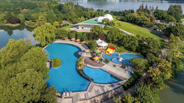 A large swimming pool with a winding design, surrounded by lush greenery and a lake. - Le Méridien Shanghai Sheshan (Shanghai)