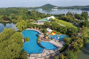 A large swimming pool with a winding design, surrounded by lush greenery and a lake. - Le Méridien Shanghai Sheshan (Shanghai)