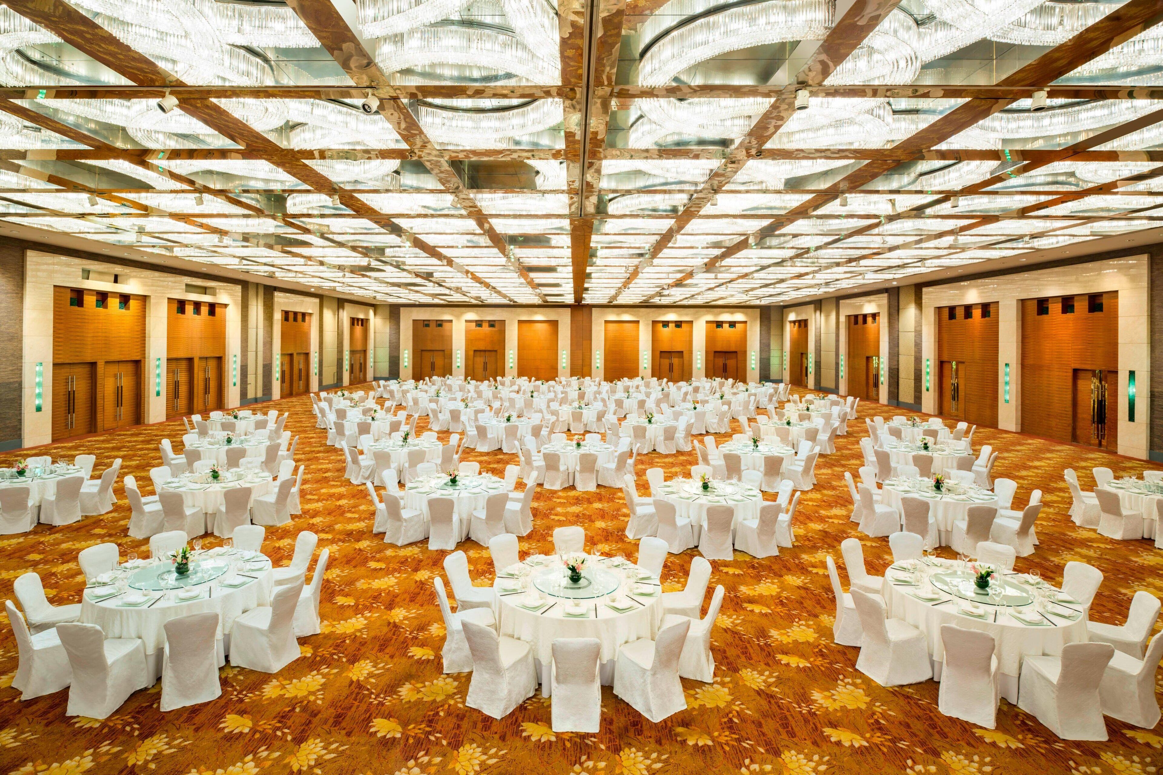 A large conference room with round tables and white chairs, a patterned carpet, and a high ceiling with wooden beams.