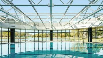 Una piscina interior con techo de cristal, ventanas amplias y vistas a un paisaje natural.