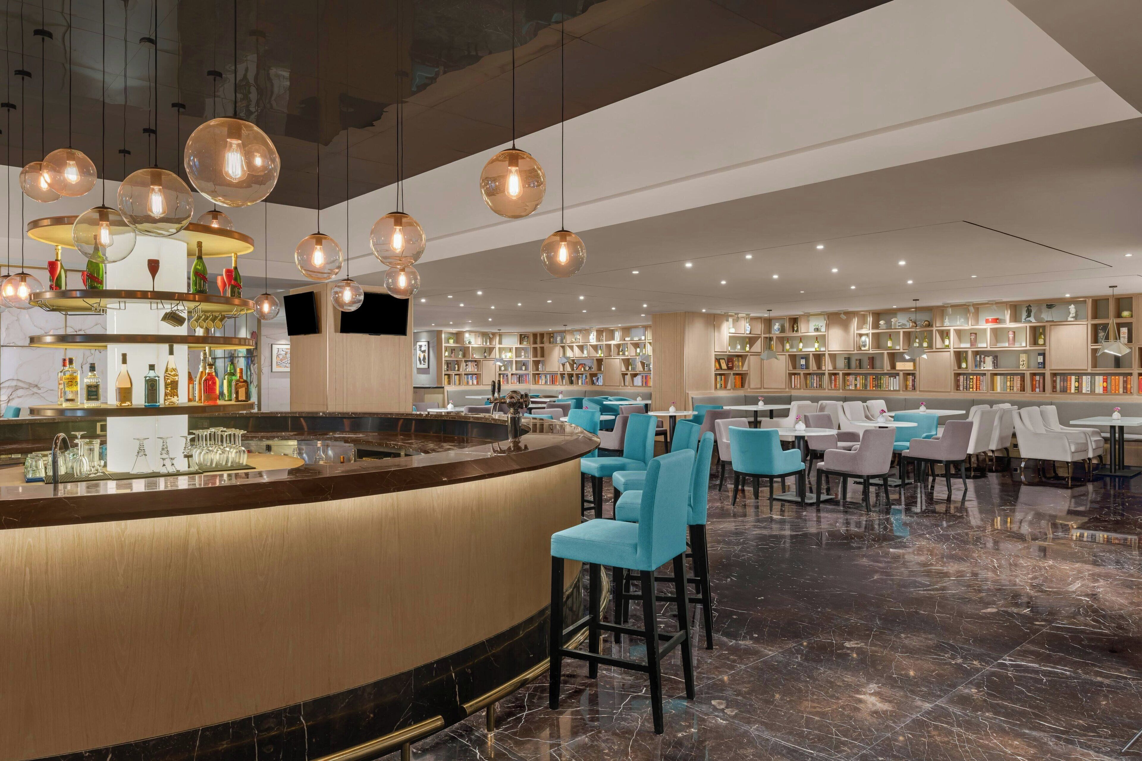 A modern bar area with a curved counter, multiple hanging light fixtures, and a variety of seating options including bar stools and tables.
