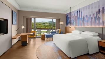A modern hotel room with a large bed, a desk, a chair, and a view of the outdoors.