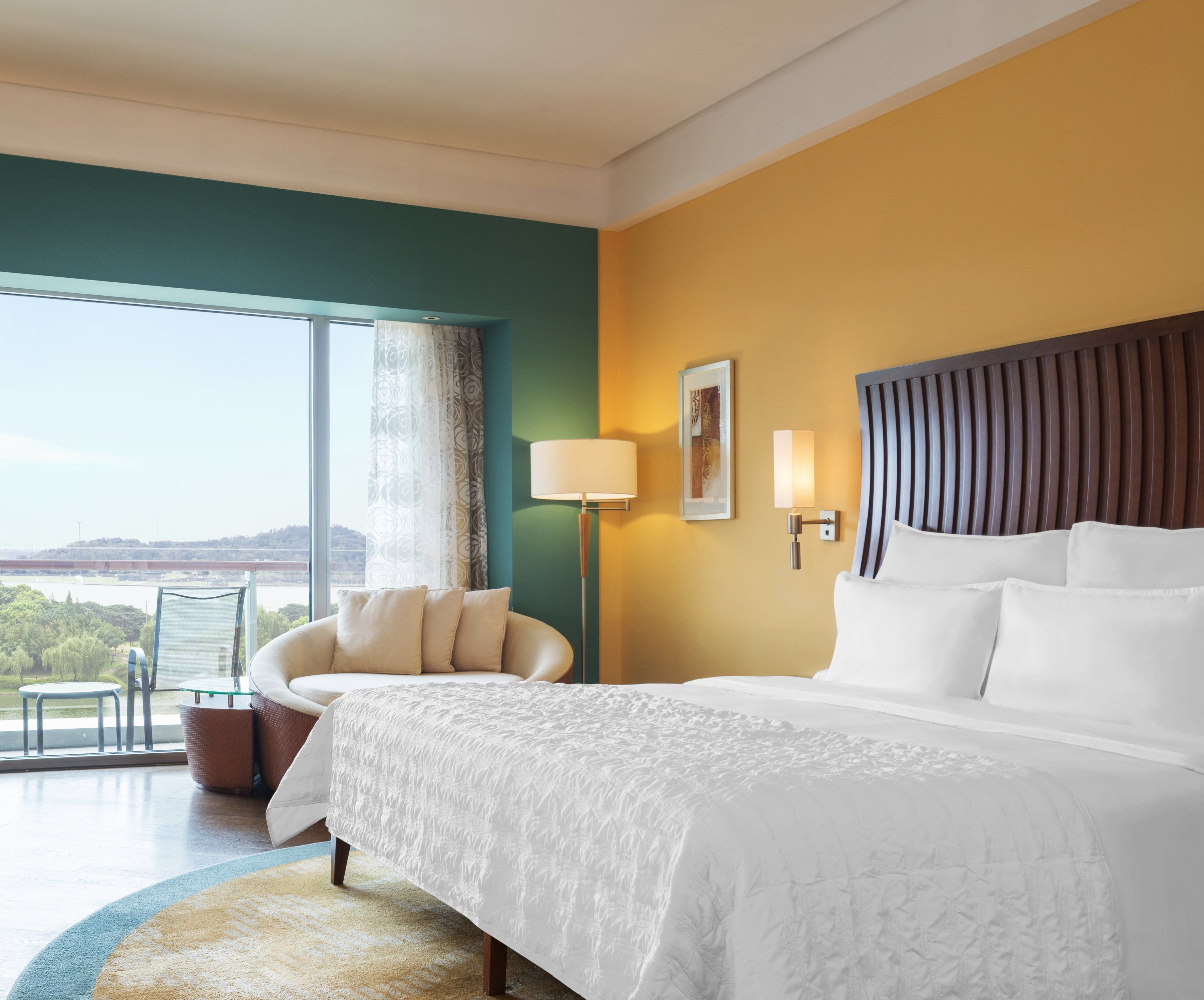 A hotel room with a large bed, a seating area with a chair, a floor lamp, and a view of a body of water.