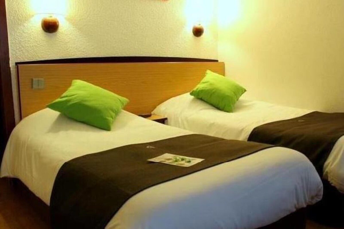 Una habitación de hotel con dos camas, cada una con un cojín verde y una colcha blanca.