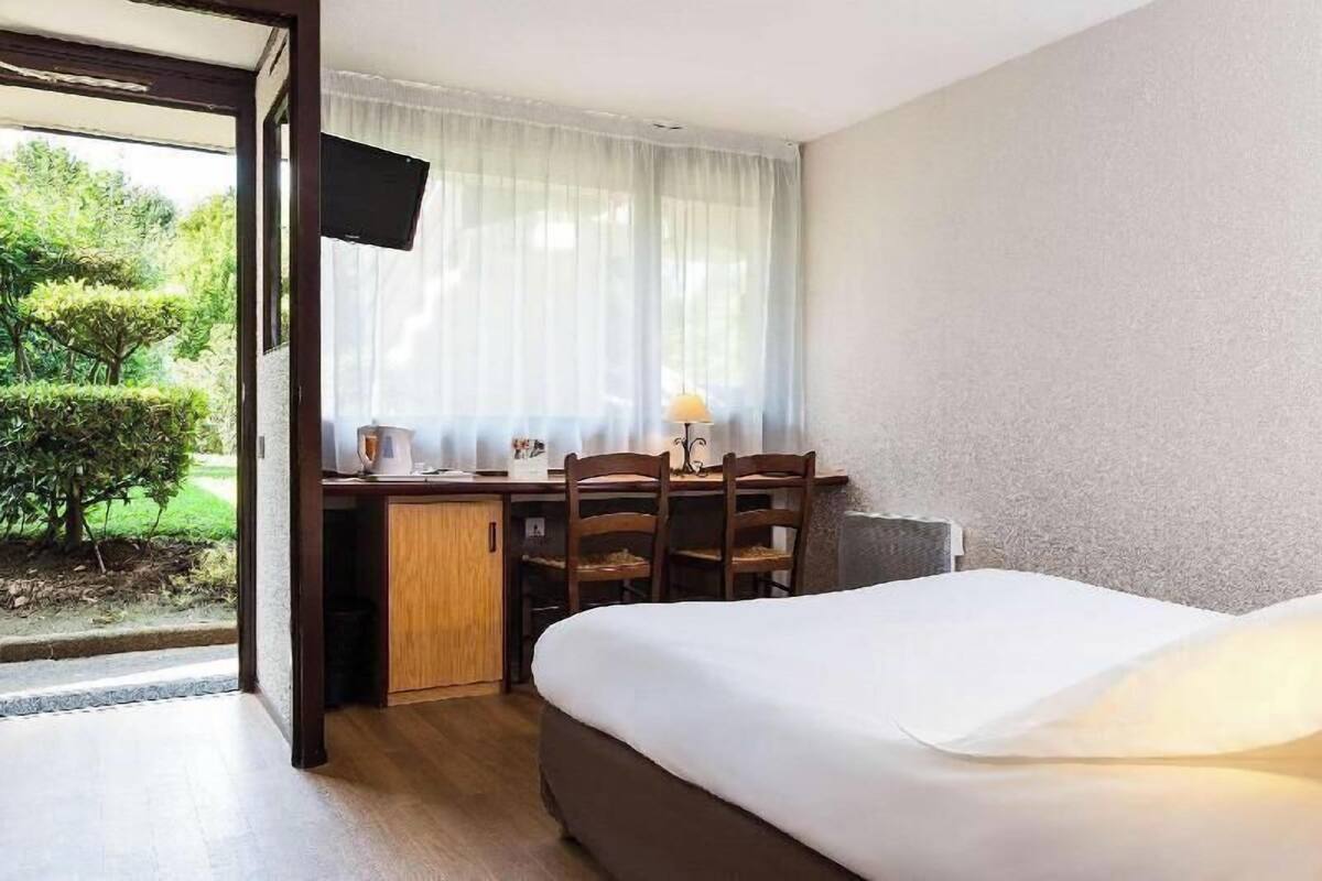 Habitación de hotel con cama, escritorio con sillas, televisor y ventana con cortinas.