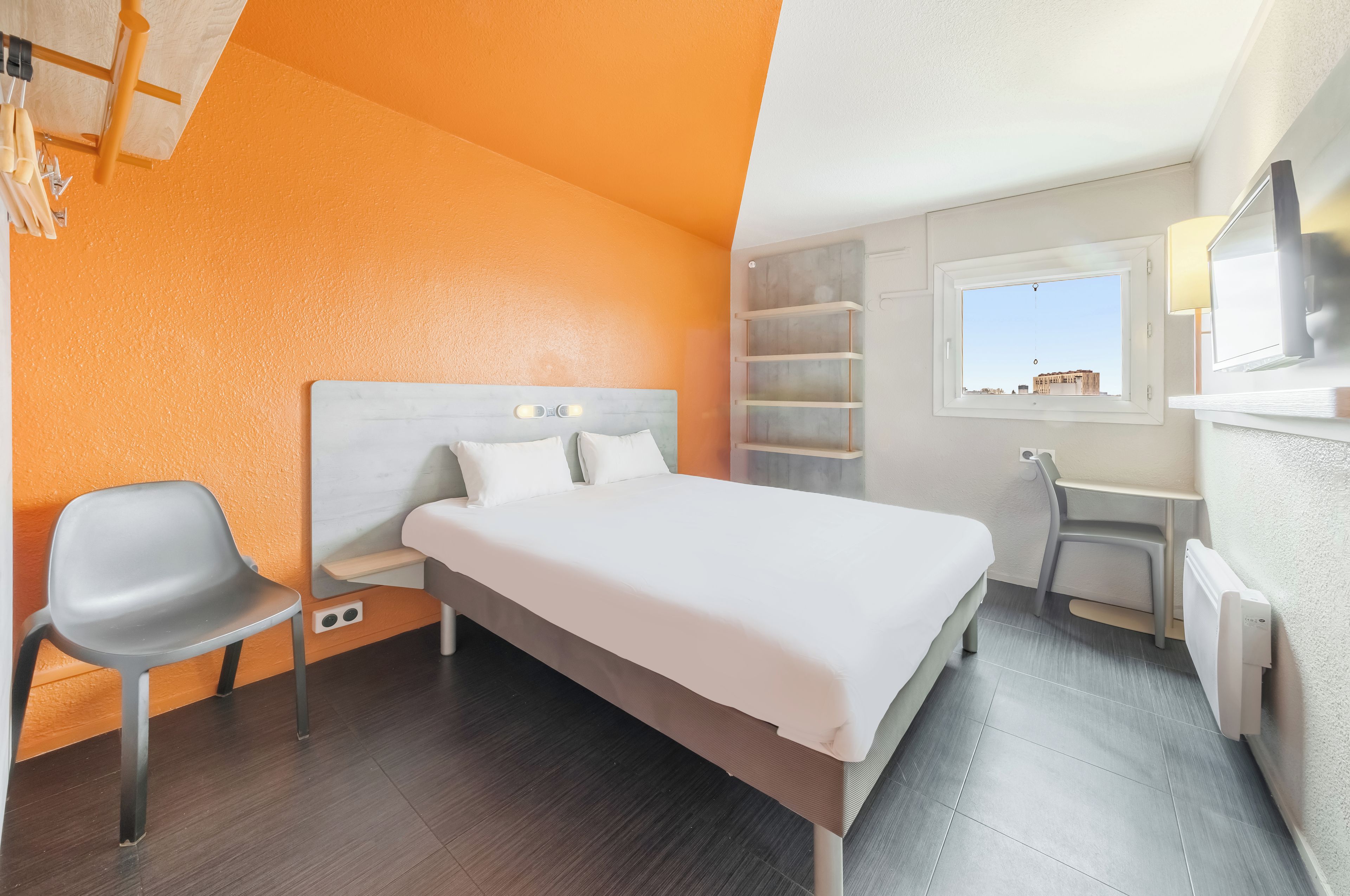 Une chambre d’hôtel avec un lit, un bureau, une chaise et une fenêtre.