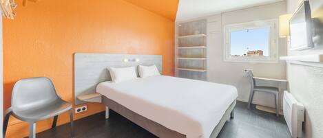 Une chambre d’hôtel avec un lit, un bureau, une chaise et une fenêtre.