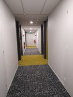 Un pasillo de hotel con alfombra estampada, paredes blancas y puertas a ambos lados.