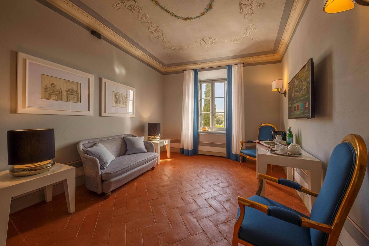 Een woonkamer met een bank, een televisie, een tafel met een lamp en een raam met gordijnen.