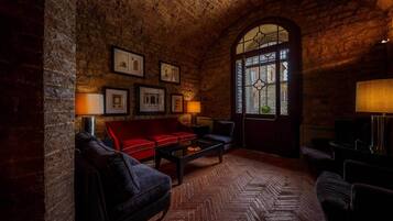 Una stanza accogliente con parete in mattoni, un divano rosso, una poltrona nera, un tavolino in legno e un'ampia finestra ad arco con vista sugli edifici.