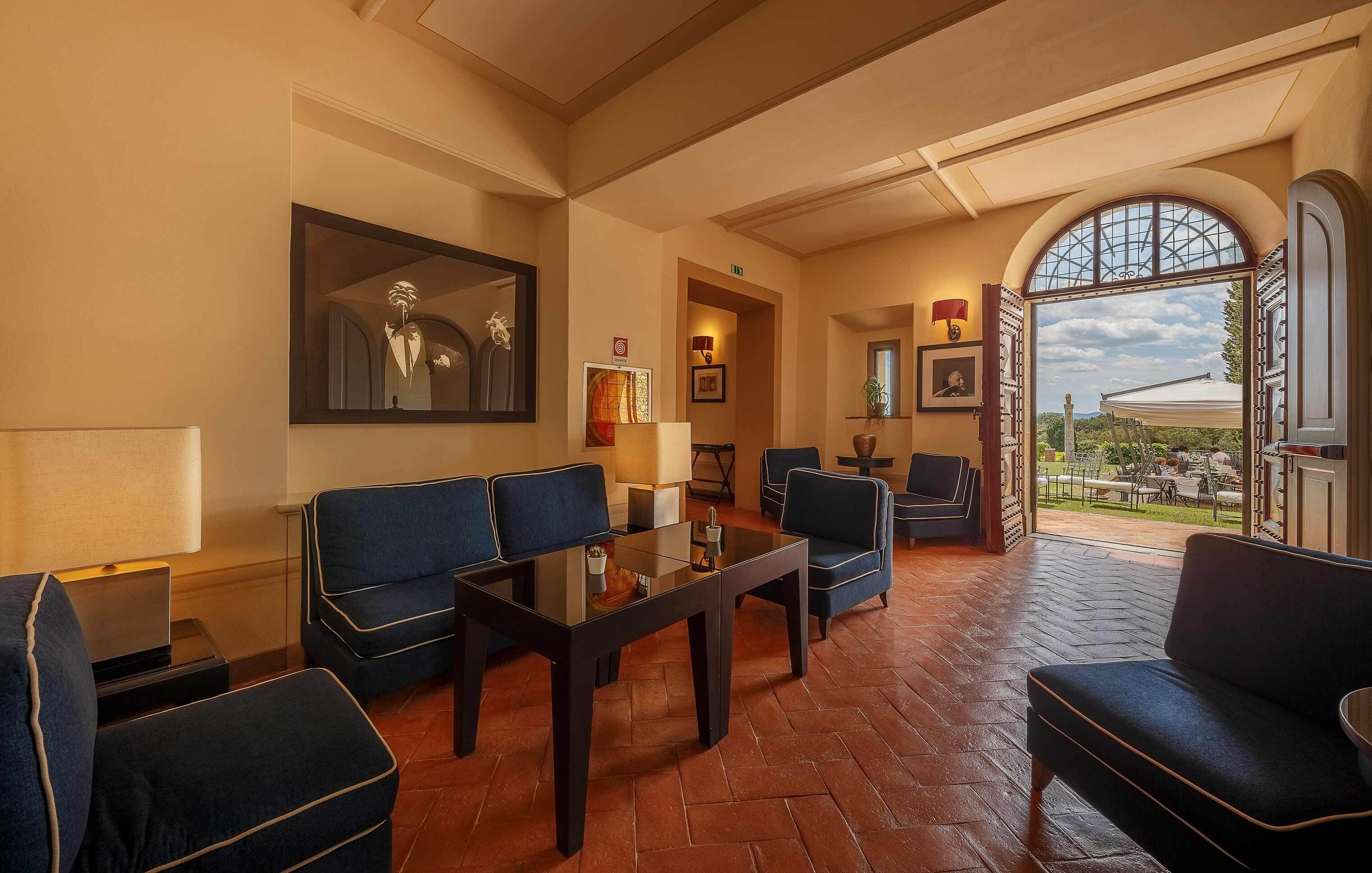 A spacious lounge with a glass table, dark blue sofas, and a large arched window offering a view of the outdoors.