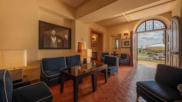A spacious lounge with a glass table, dark blue sofas, and a large arched window offering a view of the outdoors.