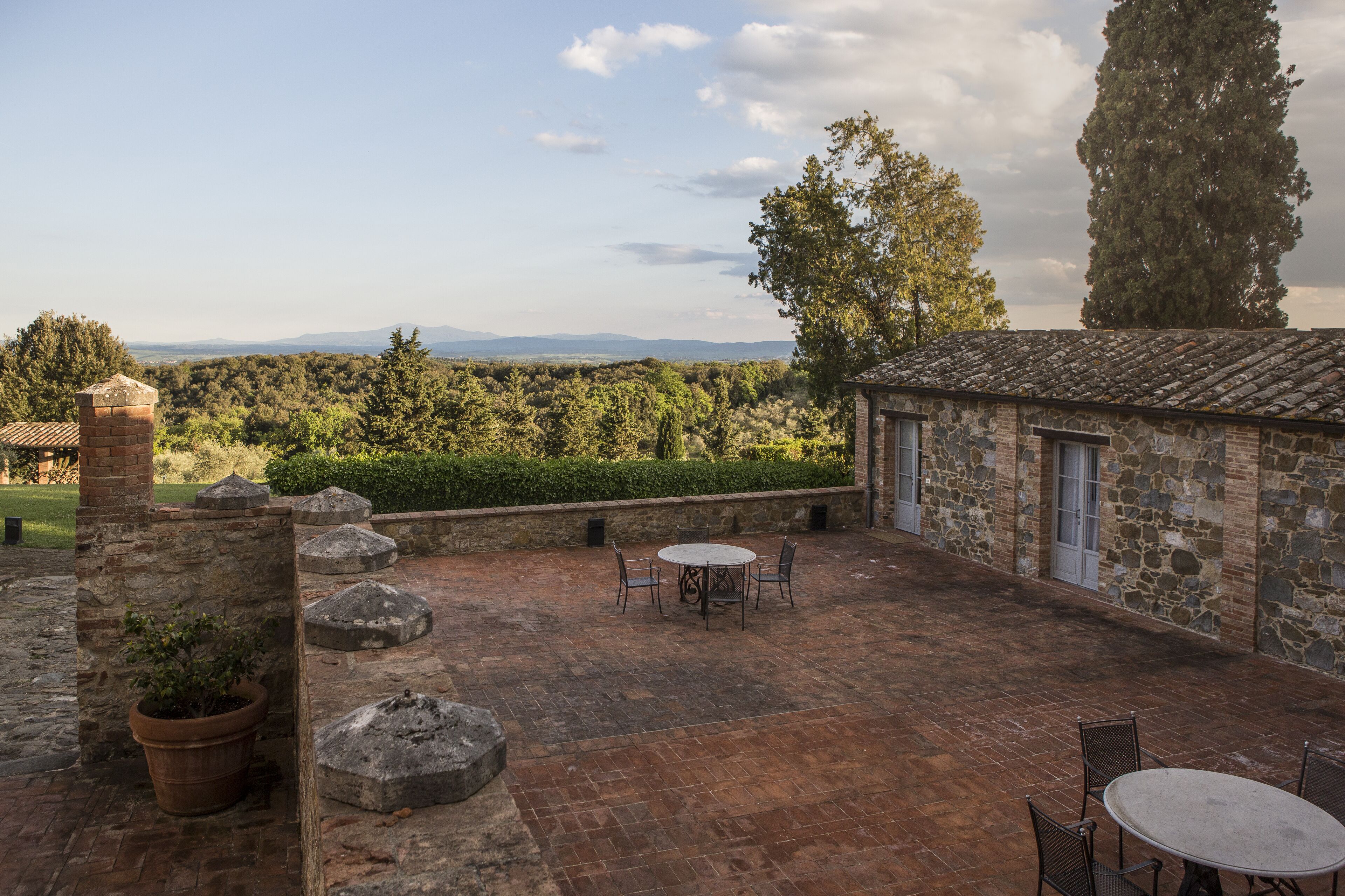 Un bâtiment en pierre doté d’un patio comprenant une table ronde et des chaises, le tout entouré de murs en pierre et de plantes en pot.
