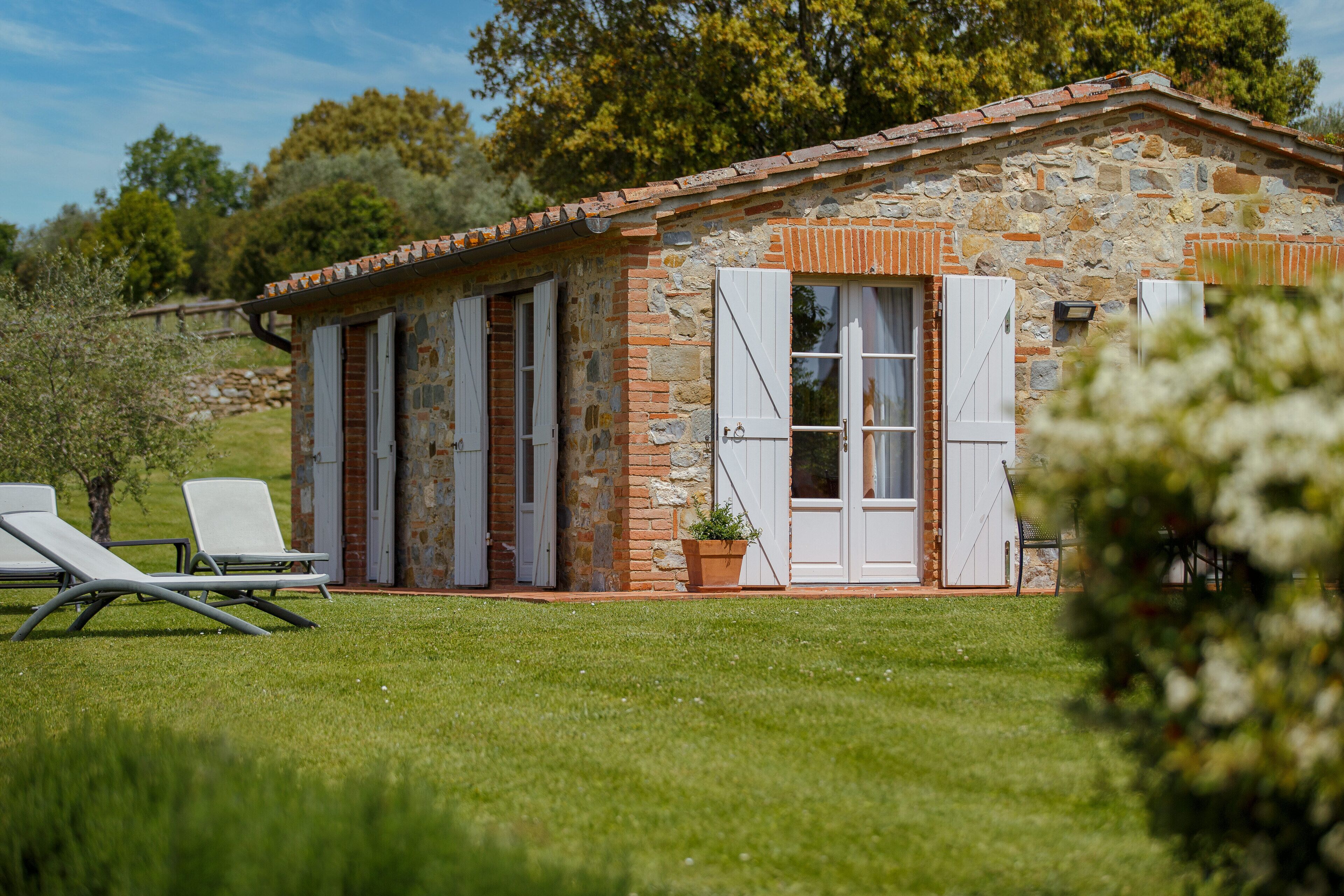A stone building with white shutters, a small porch, and two lounge chairs.