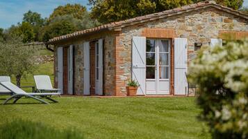 A stone building with white shutters, a small porch, and two lounge chairs.