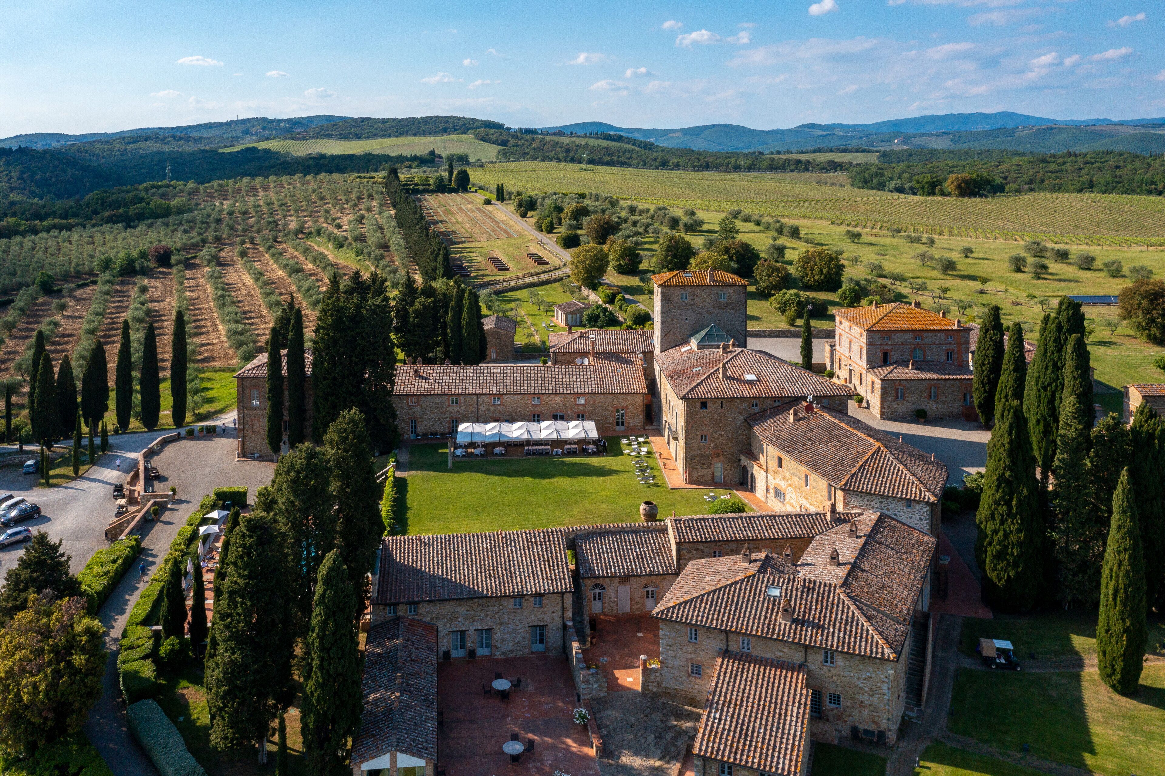Un edificio storico con un cortile, circondato da vigneti e dolci colline.