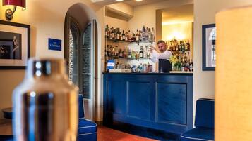 Un espace bar avec un barman, des étagères remplies de bouteilles d’alcool et des sièges bleus.
