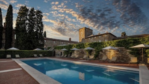 Una piscina con sillones de descanso y sombrillas, rodeada de edificios de piedra y árboles.