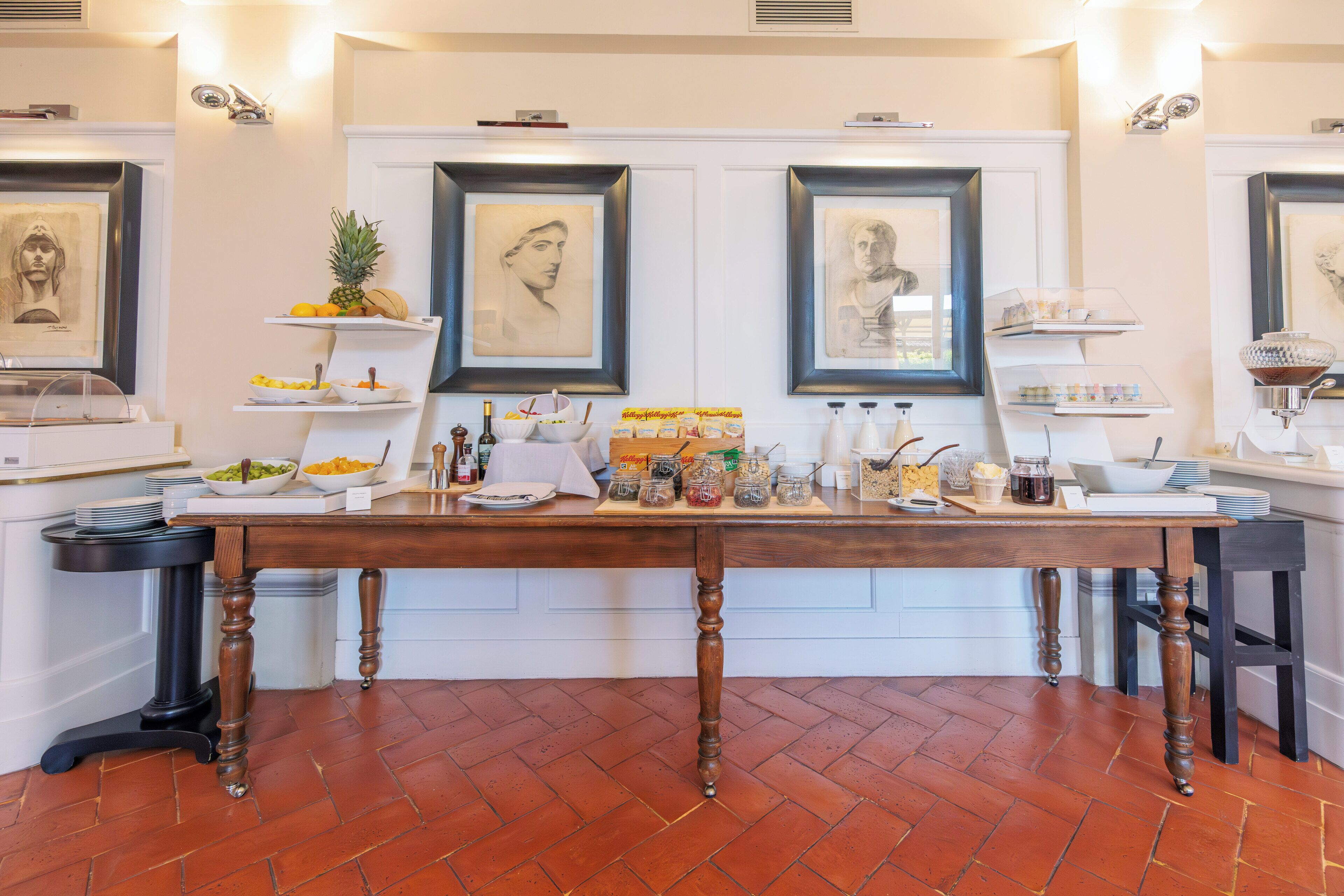 Une table à manger avec de la nourriture et des boissons, des œuvres d’art encadrées accrochées au mur et un sol carrelé.