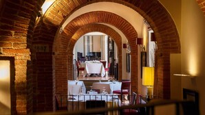 Un corredor de ladrillo abovedado que conduce a un comedor con mesas dispuestas para una comida.
