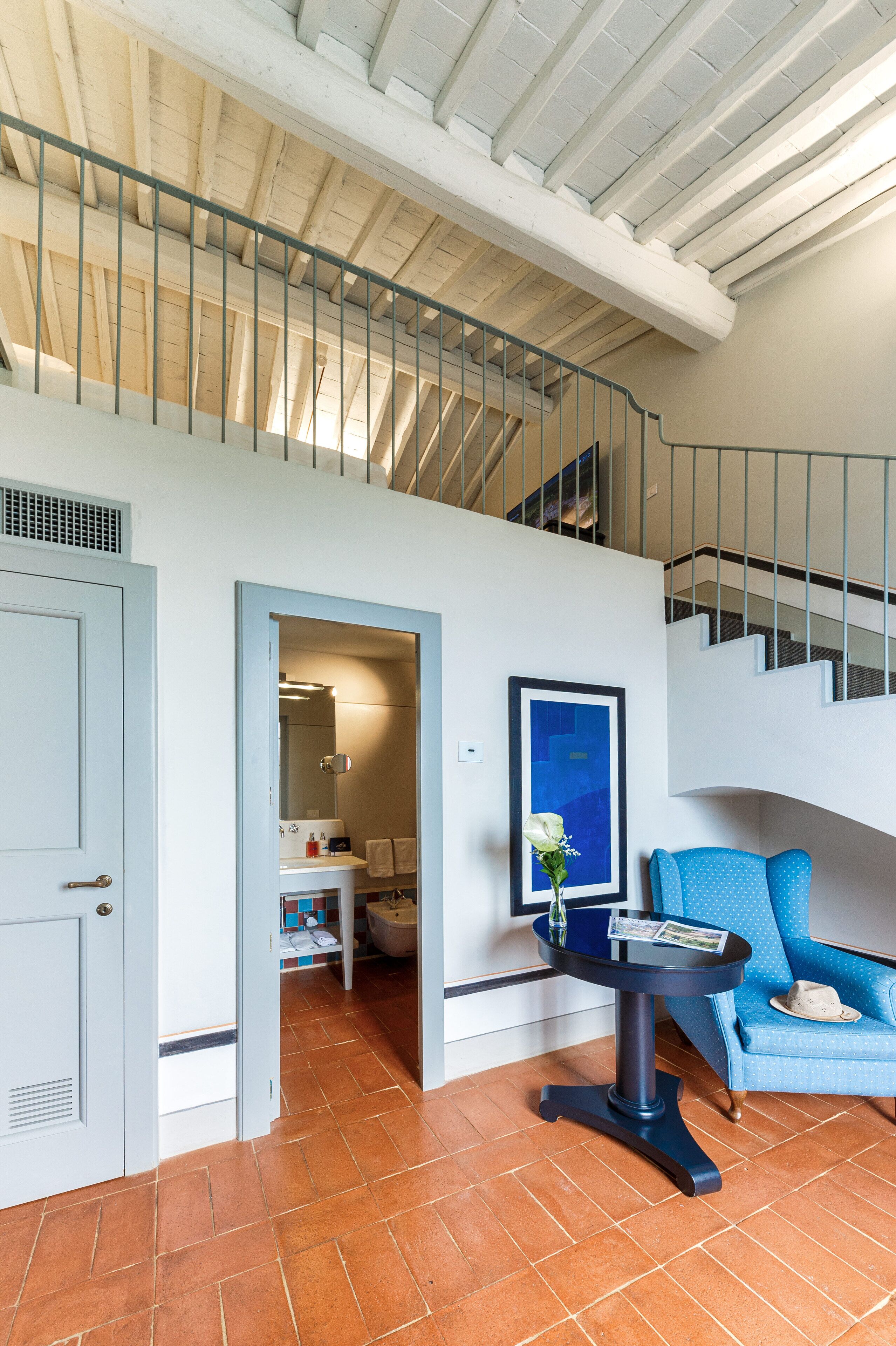 A spacious room with a staircase, a blue sofa, and a small table with a vase.