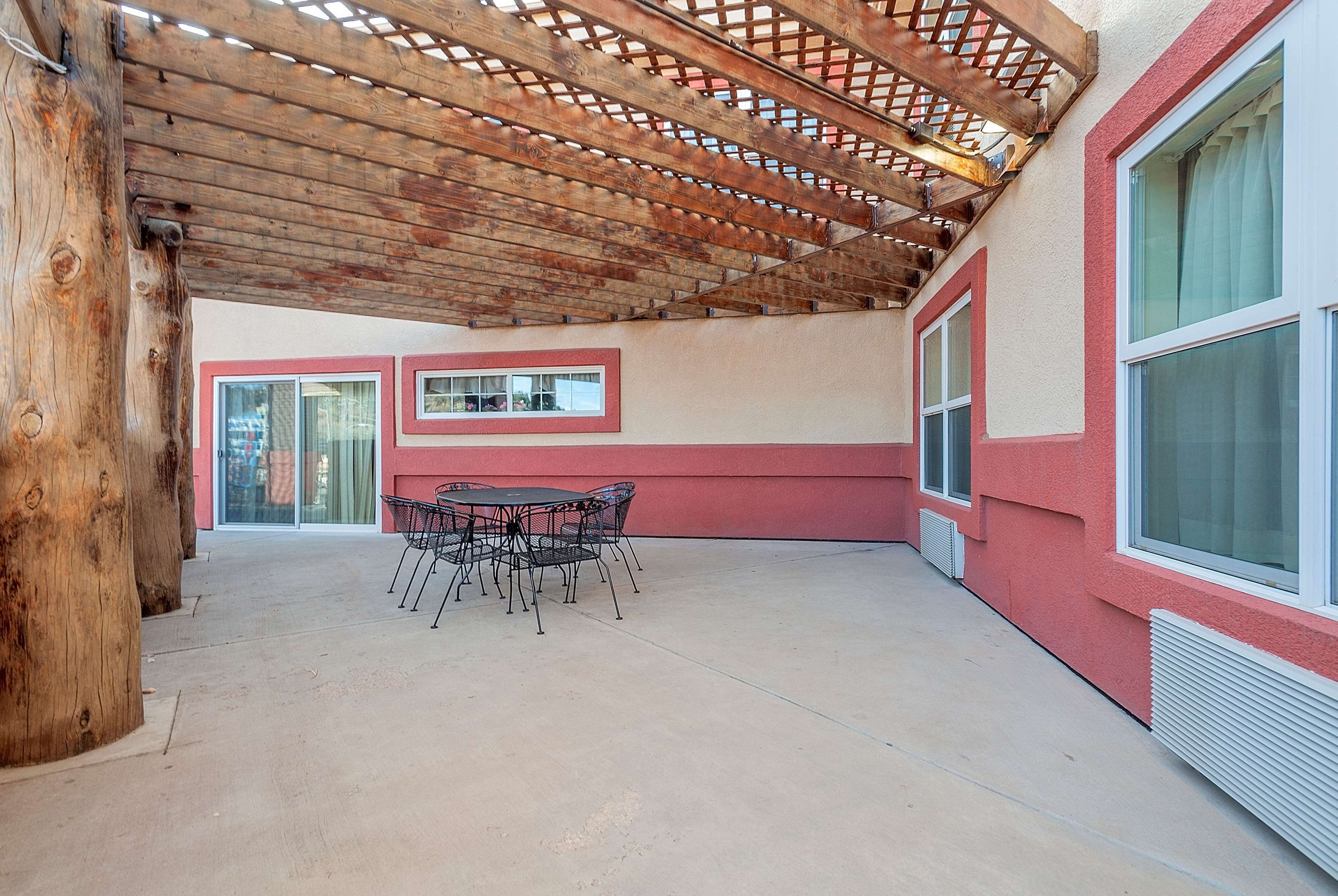 Ein überdachter Patio-Bereich mit einer Holzw pergola, einem Tisch mit Stühlen und einem rot-weißen Gebäude mit großen Fenstern.