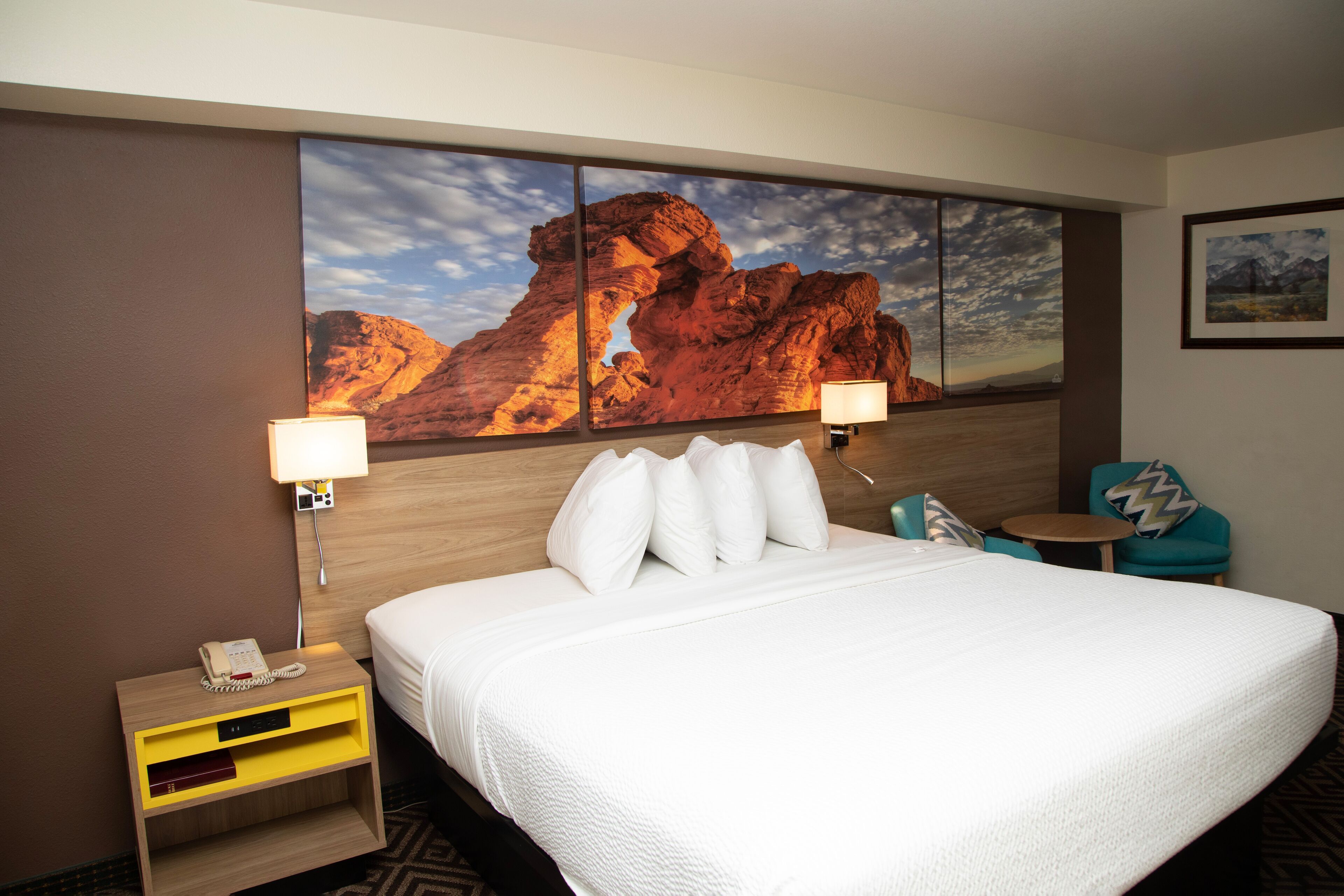 Ein Hotelzimmer mit einem großen Bett, zwei Nachttischlampen, einem Nachttisch mit Telefon, einem kleinen Tisch und einem Sessel.