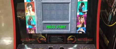 Une borne d’arcade ancienne pour le jeu Mortal Kombat II, dotée de plusieurs boutons de contrôle et d’un écran affichant la mention « JEU GRATUIT ».