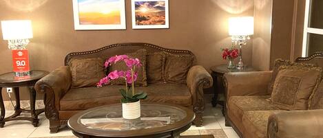 A living room with a brown sofa, a glass coffee table with pink orchids, and framed pictures on the wall.