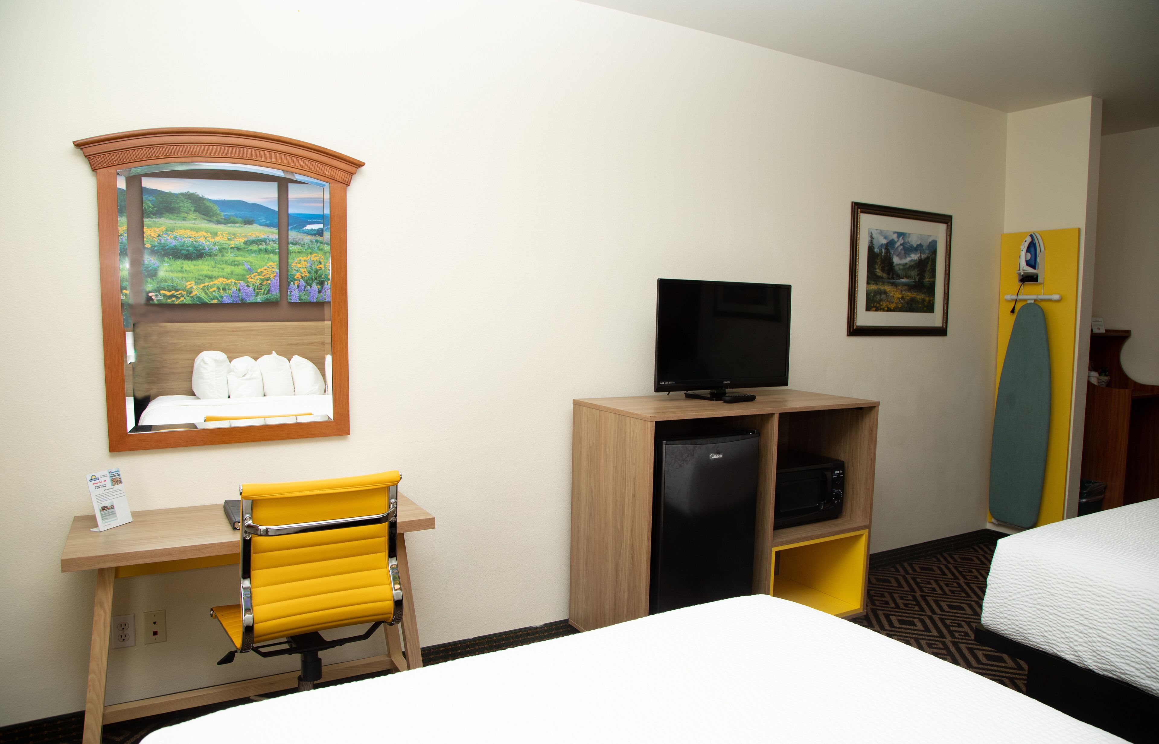 A hotel room with a bed, a desk with a chair, a television, a refrigerator, and a window with a view of a landscape.