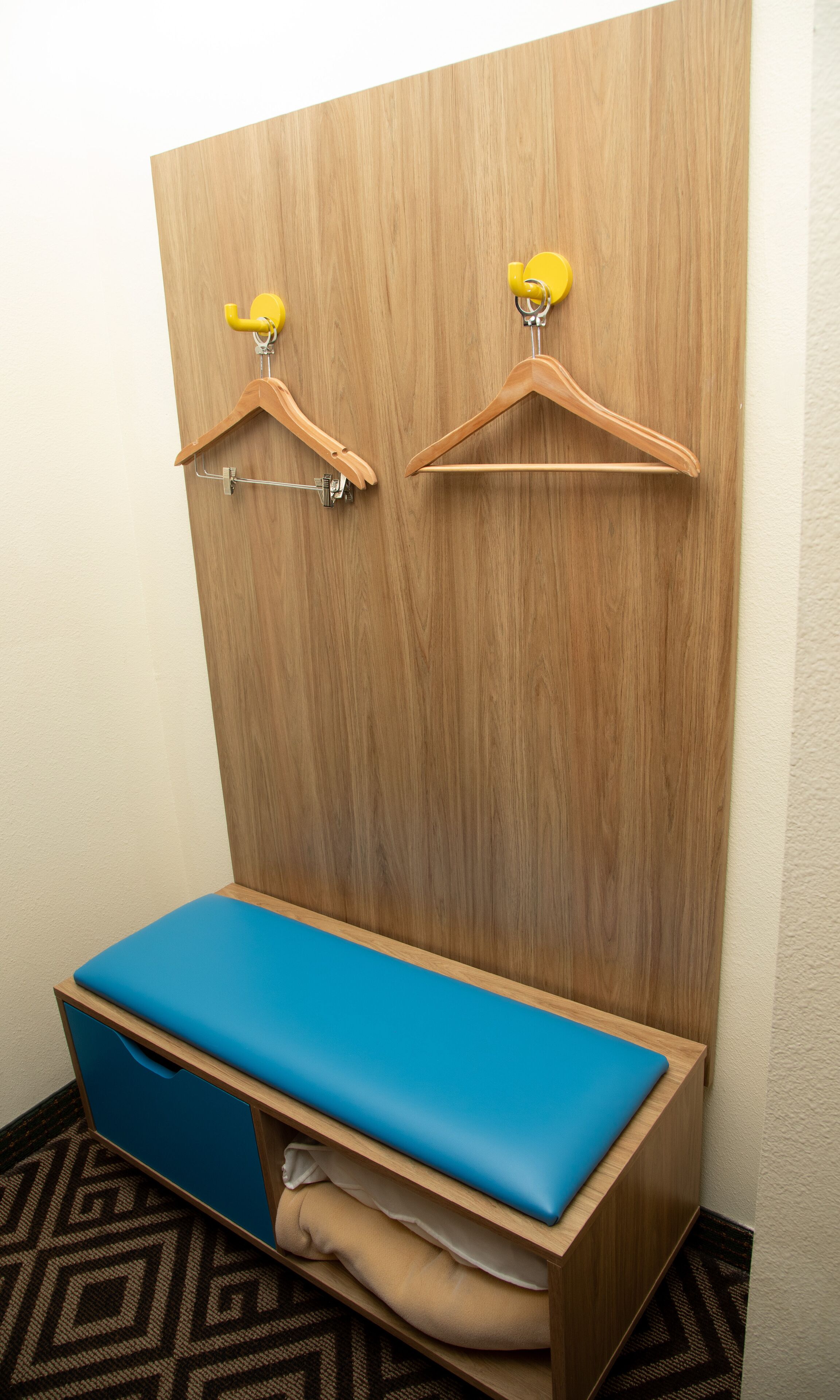 A wooden wardrobe with two yellow hangers and a blue bench.