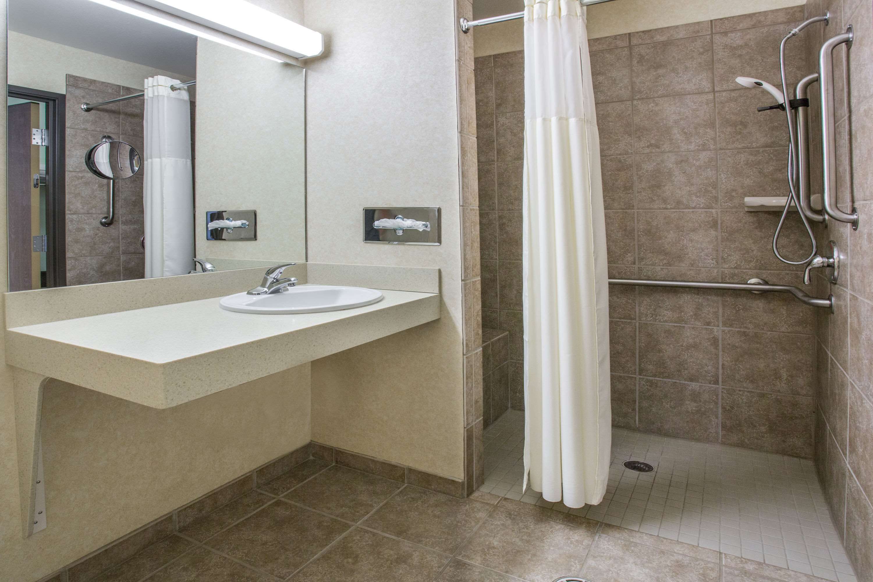 A modern bathroom with a sink, mirror, shower, and grab bars.