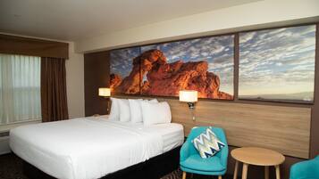 A hotel room with a large bed, a desk, two chairs, and a large rock painting on the wall.