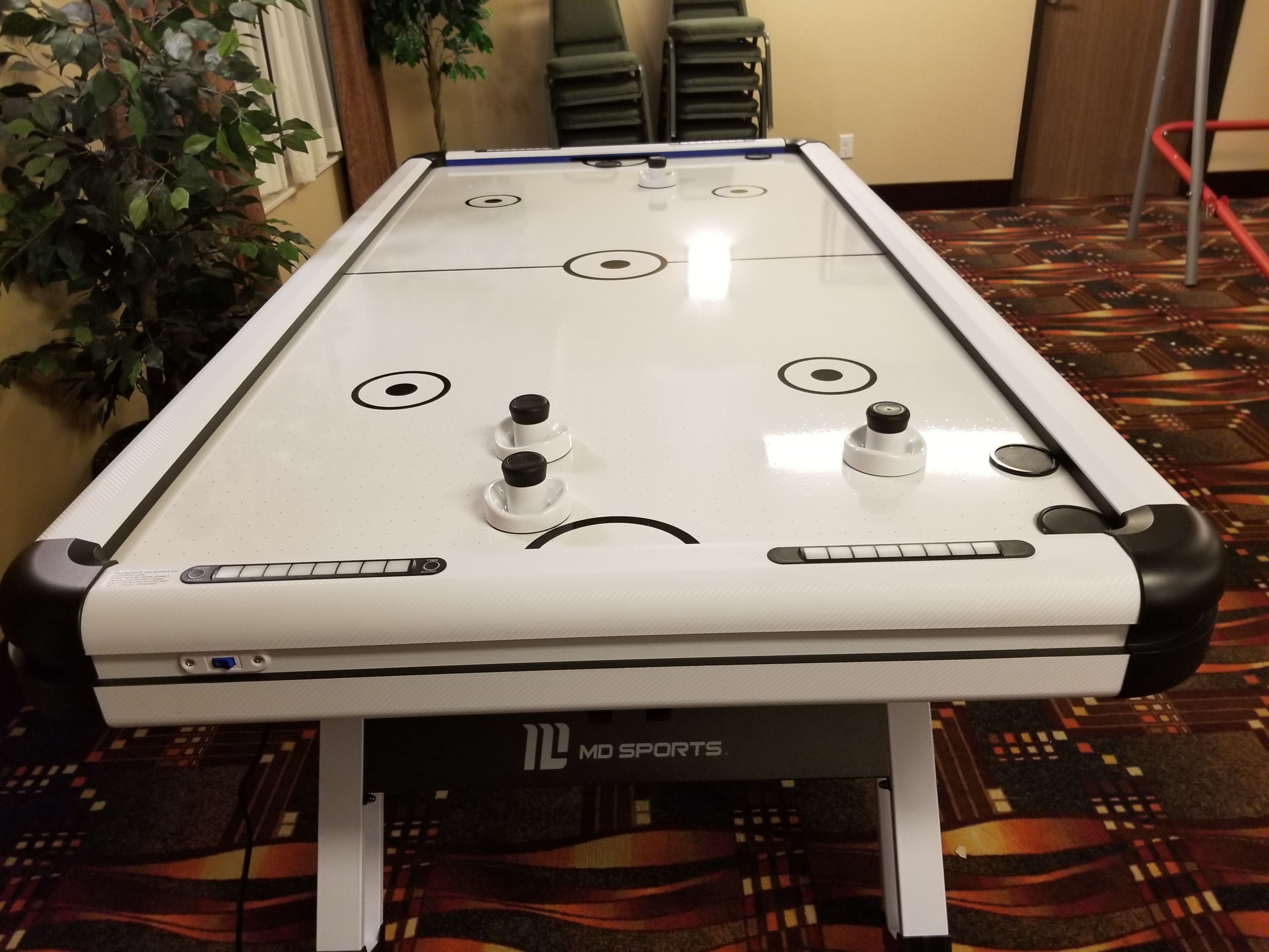 A pool table with MD Sports branding, surrounded by chairs and a patterned carpet.