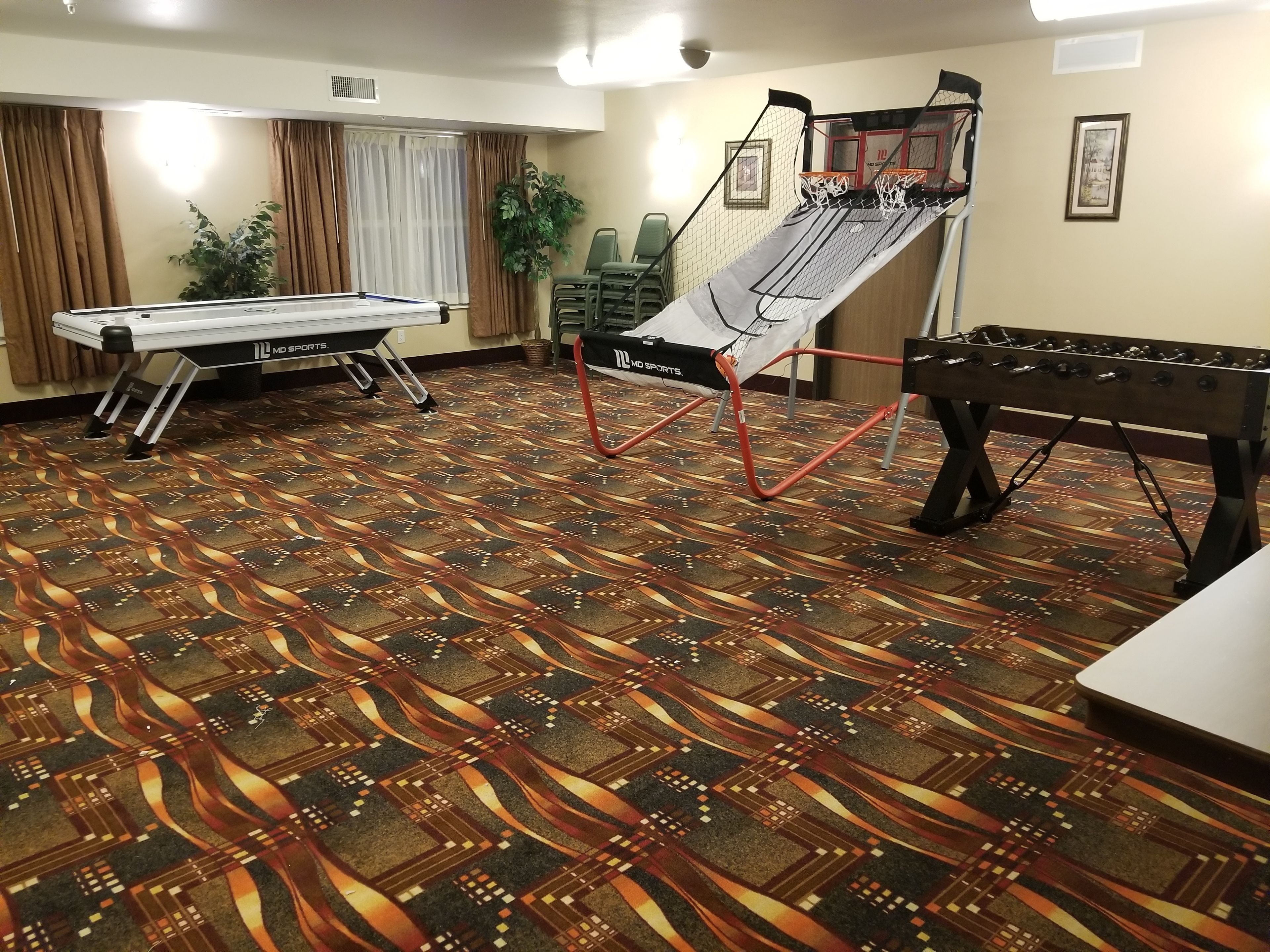 A room with a pool table, a foosball table, and a basketball hoop.