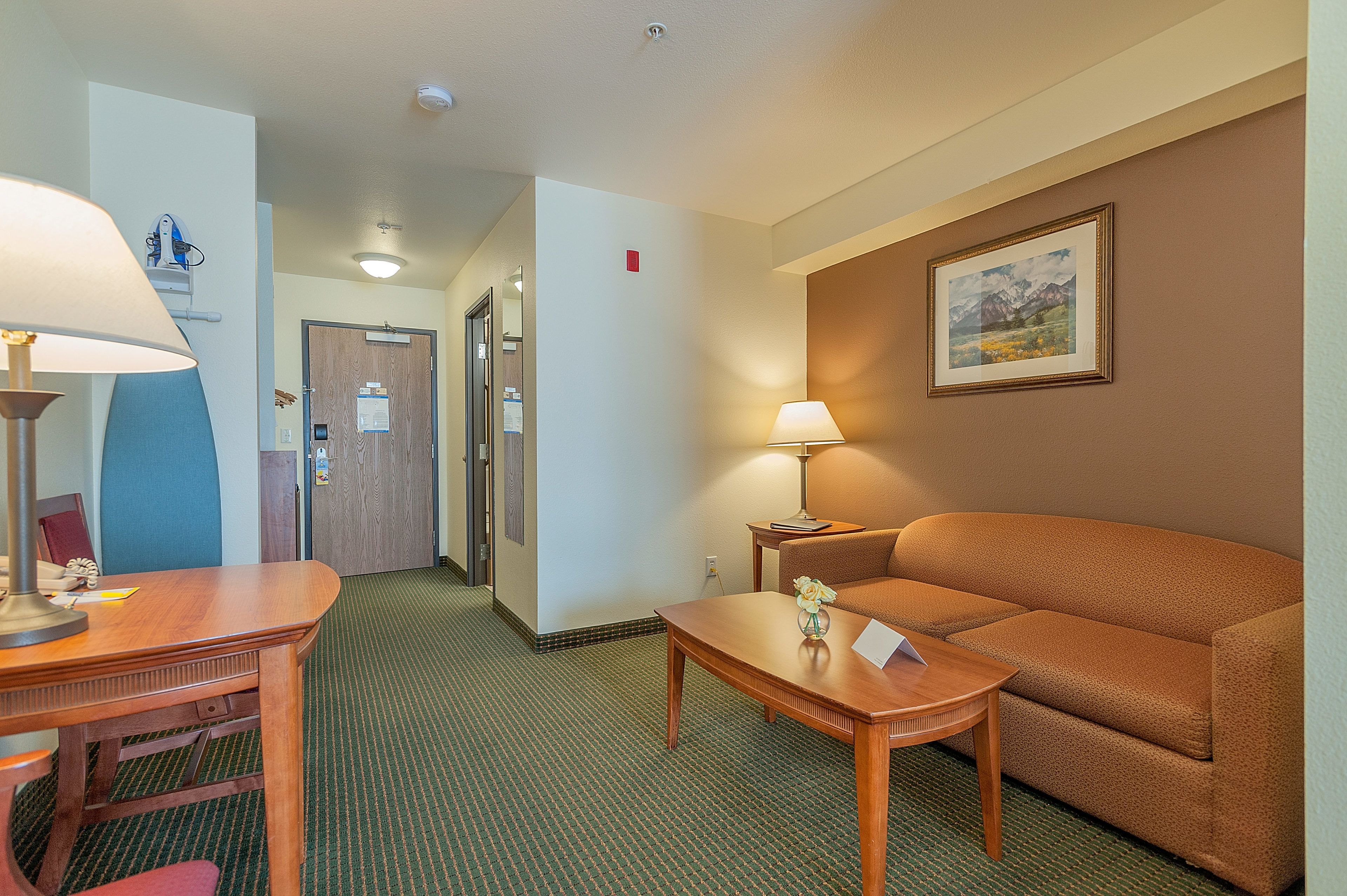 A hotel room with a wooden desk, a sofa, a lamp, and a framed picture on the wall.