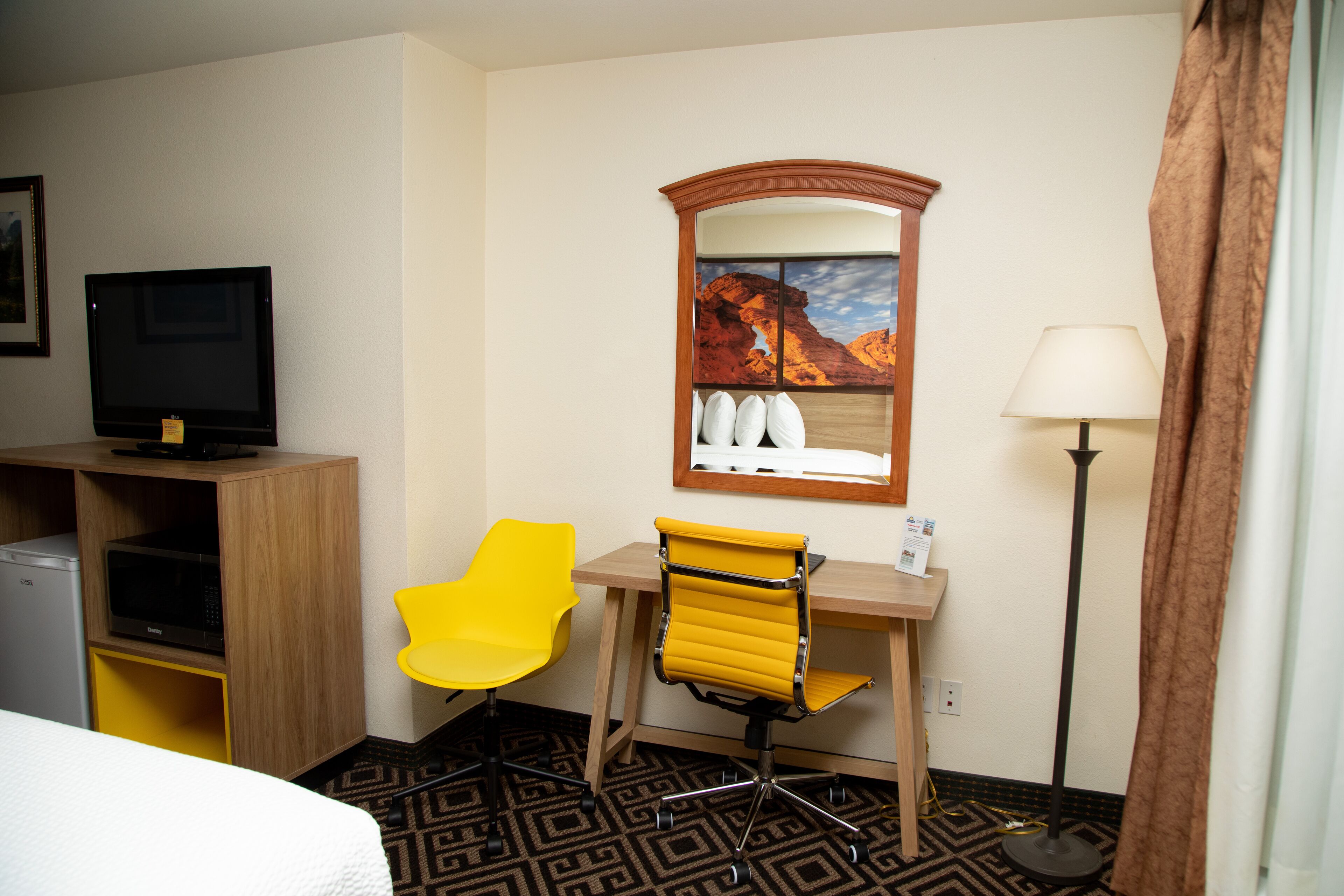 Une chambre d’hôtel comprenant un lit, un bureau avec une chaise, une télévision, un four à micro-ondes, une lampe et une fenêtre donnant sur une vue sur la montagne.