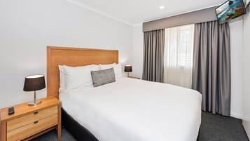 A neatly made bed with a wooden headboard, a nightstand with a lamp, and a TV mounted on the wall.