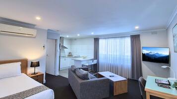 Habitación de hotel con cama, sofá, escritorio, televisor y zona de cocina.