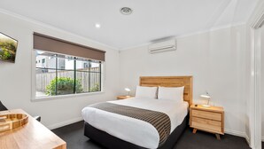 A modern hotel room with a large bed, a wooden nightstand, a desk, and a window with a view of the outside. - Fawkner Executive Suites & Serviced Apartments (Fawkner)