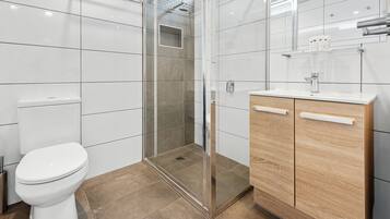 Un baño moderno con ducha de vidrio, inodoro blanco y tocador de madera con lavamanos.