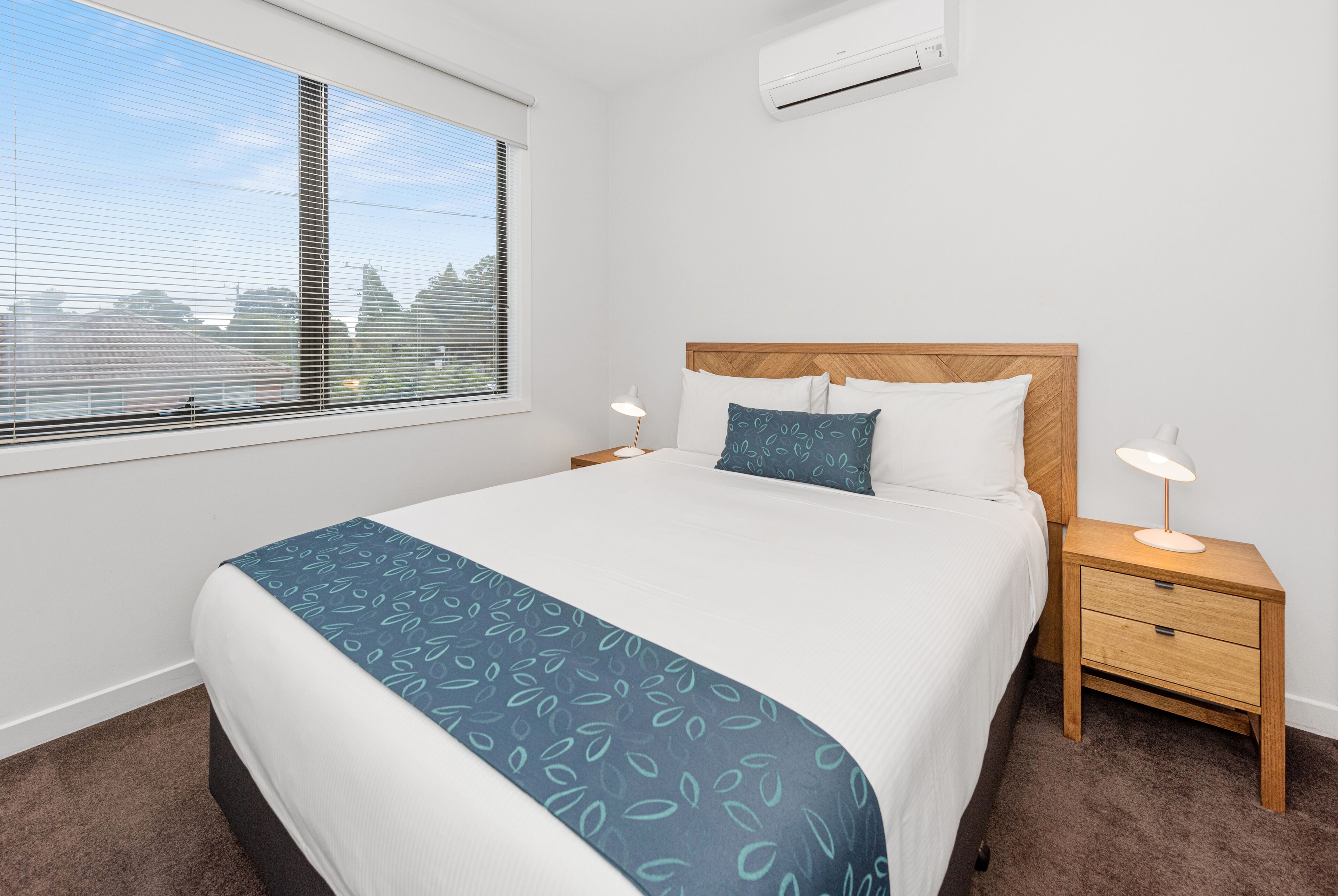 A neatly made bed with a blue patterned bedspread, a wooden headboard, and two bedside lamps.