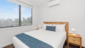 A neatly made bed with a blue patterned bedspread, a wooden headboard, and two bedside lamps.