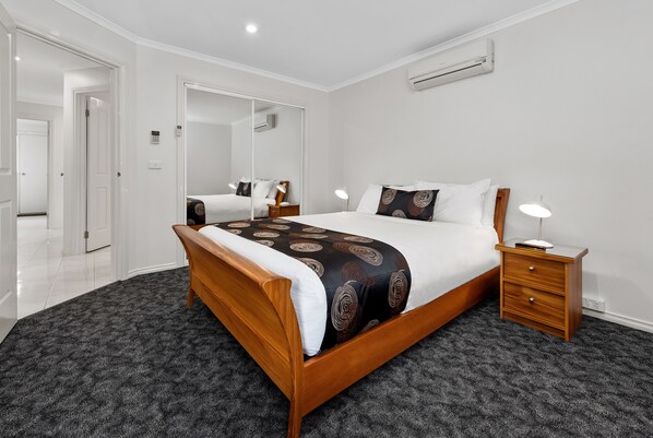 A bedroom with a wooden bed, a bedside table, a mirror, and a carpeted floor.