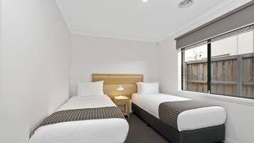A small hotel room with two single beds, a nightstand with a lamp, and a window with a view of a wooden fence.