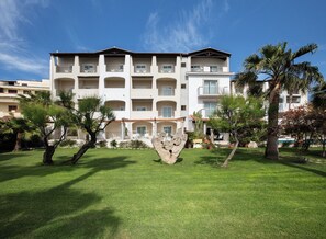 A multi-story hotel with balconies, a well-maintained lawn, and palm trees.